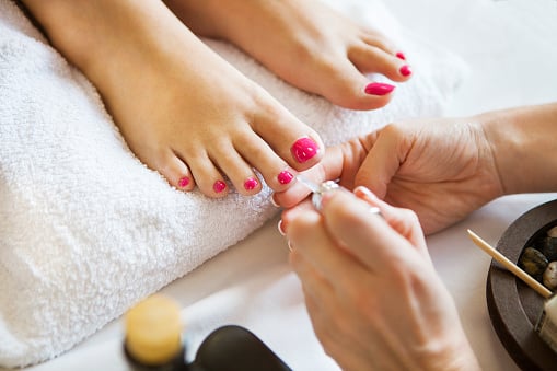 Woman in nail salon, receiving pedicure by beautician. Close up of female feet resting on white towel
