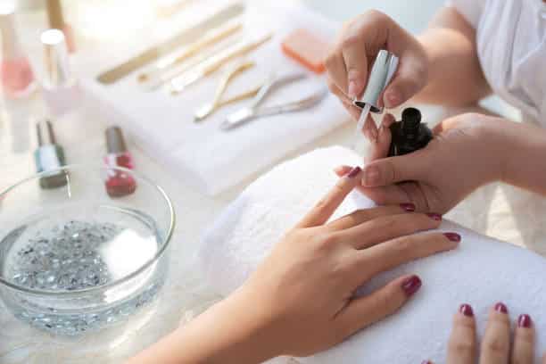 woman having manicure, applying red nail polish, lying manicure kit tools on towel