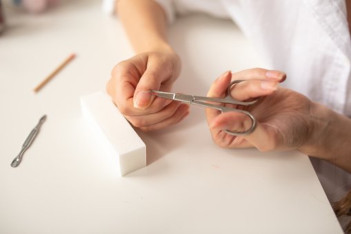 Cuticle scissors, Young woman cutting cuticle with nail scissors at home