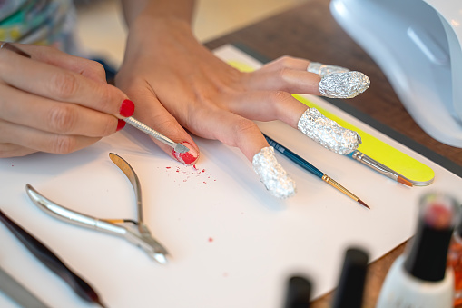 Removing gel nail polish from hand fingers with foil, red gel polish, beauty with nail tools